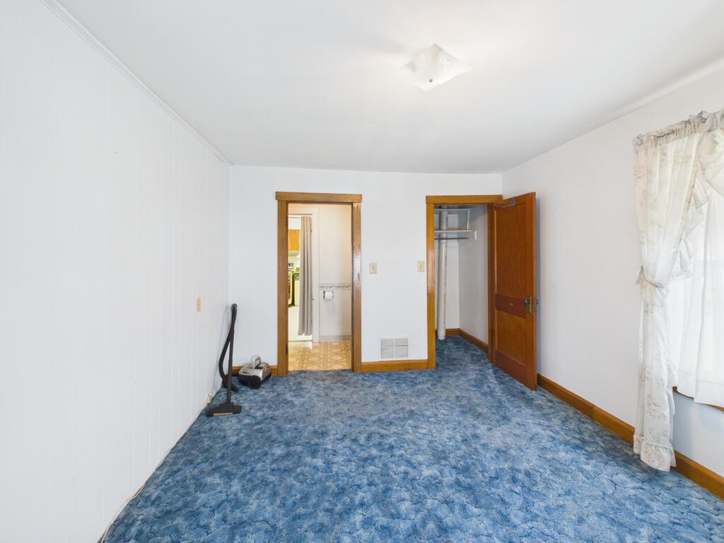 Empty bedroom with blue patterned carpet, wooden closet door, and curtained window.