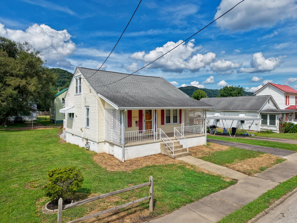 Pale yellow house with a covered porch, red shutters, and a concrete walkway across the lawn.