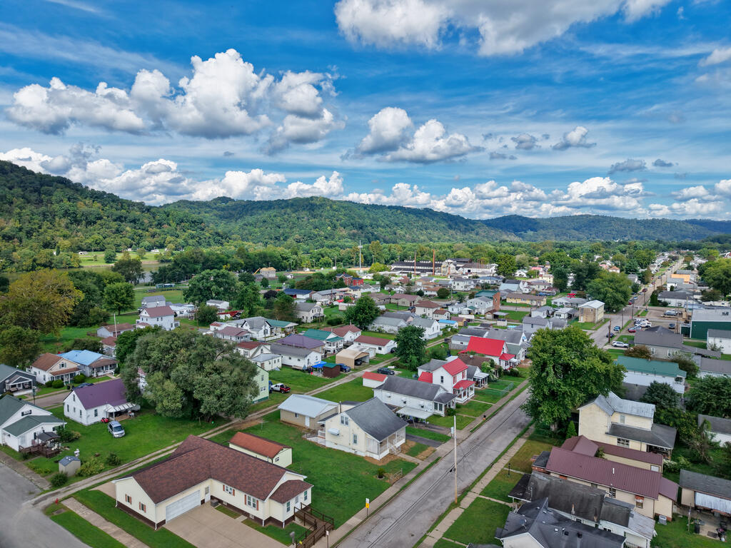 Aerial view of a residential neighborhood among wooded hills under a bright, cloud-filled sky.