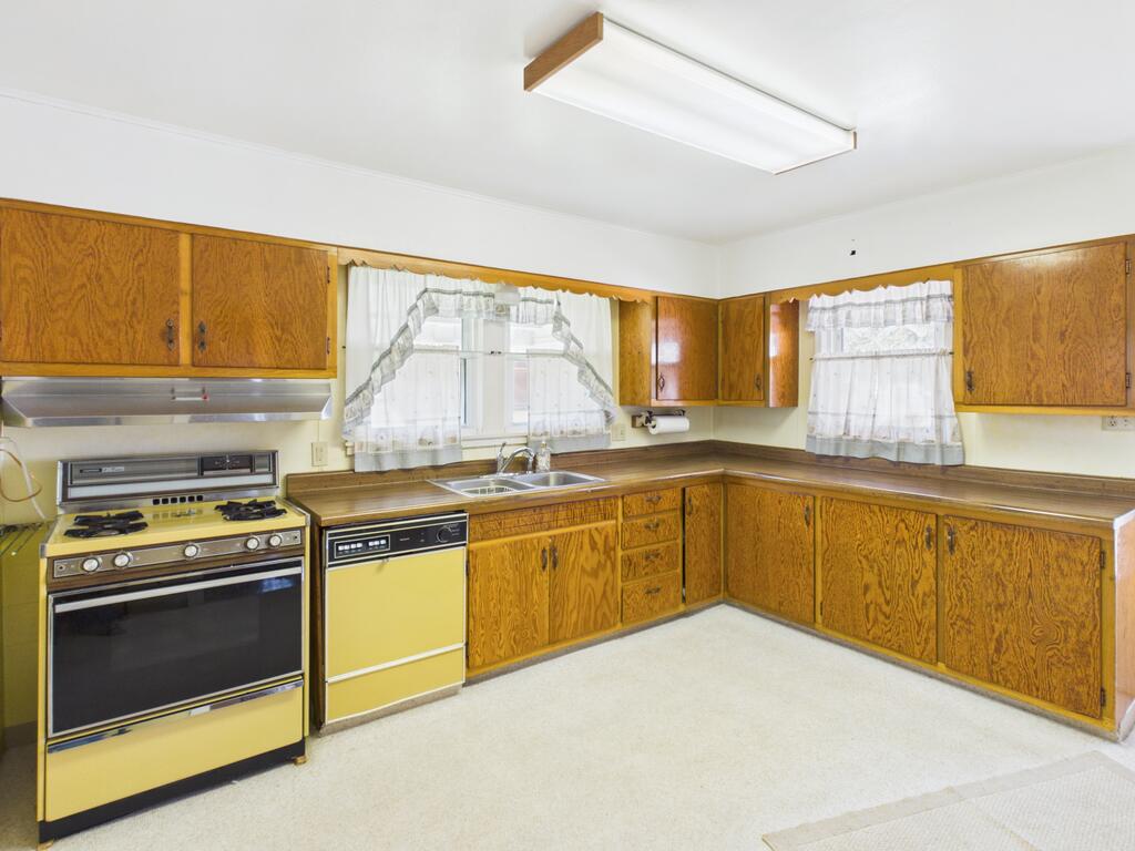 Kitchen with golden-brown wood cabinets, a yellow range and dishwasher, and curtained windows.
