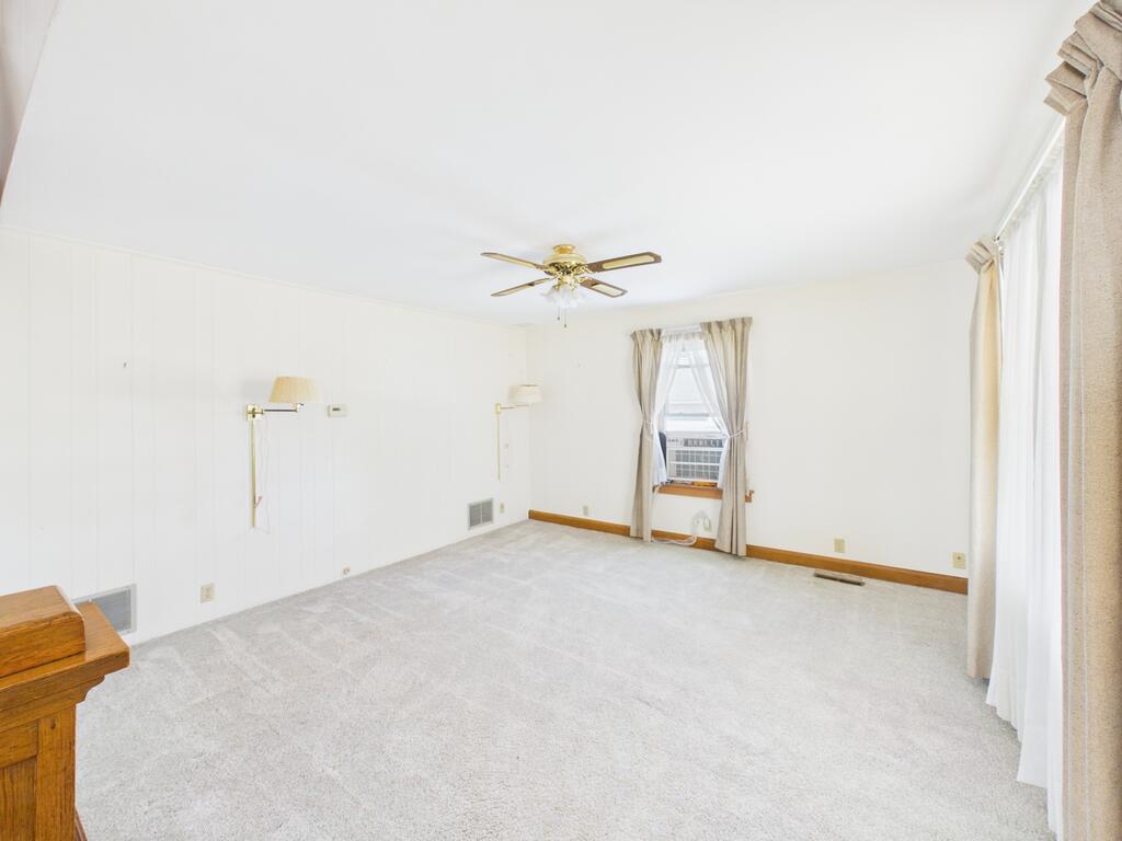 Mostly empty carpeted room with a ceiling fan, wall lamps, and a window air conditioner.