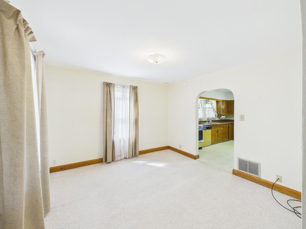 Empty carpeted living room with an arched opening to the kitchen and wood trim.