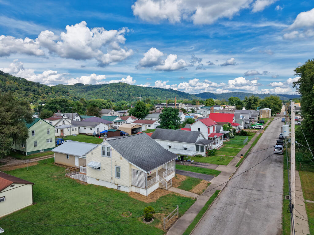 Aerial view of a residential neighborhood, with a quiet street and green hills beyond.