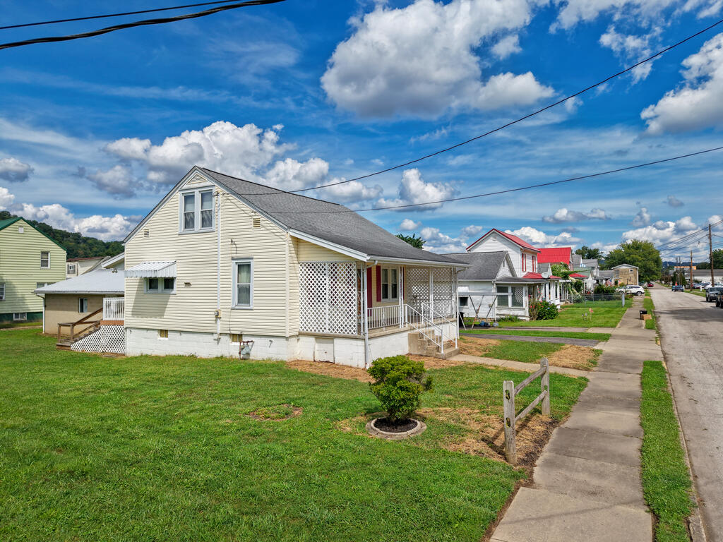 Cream-sided house with a gray roof, lattice porch, and small front lawn beside a sidewalk.
