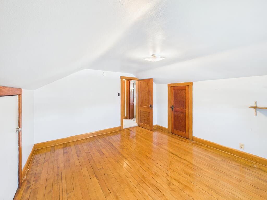 Empty room with hardwood floors, a sloped ceiling, and several wood-trimmed doors.