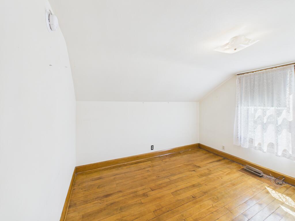 Empty room with hardwood floors, wood baseboards, and a lace-curtained window.