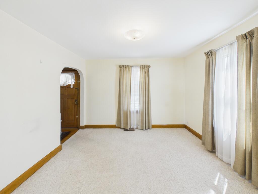 Vacant carpeted room with curtained windows and an arched doorway.