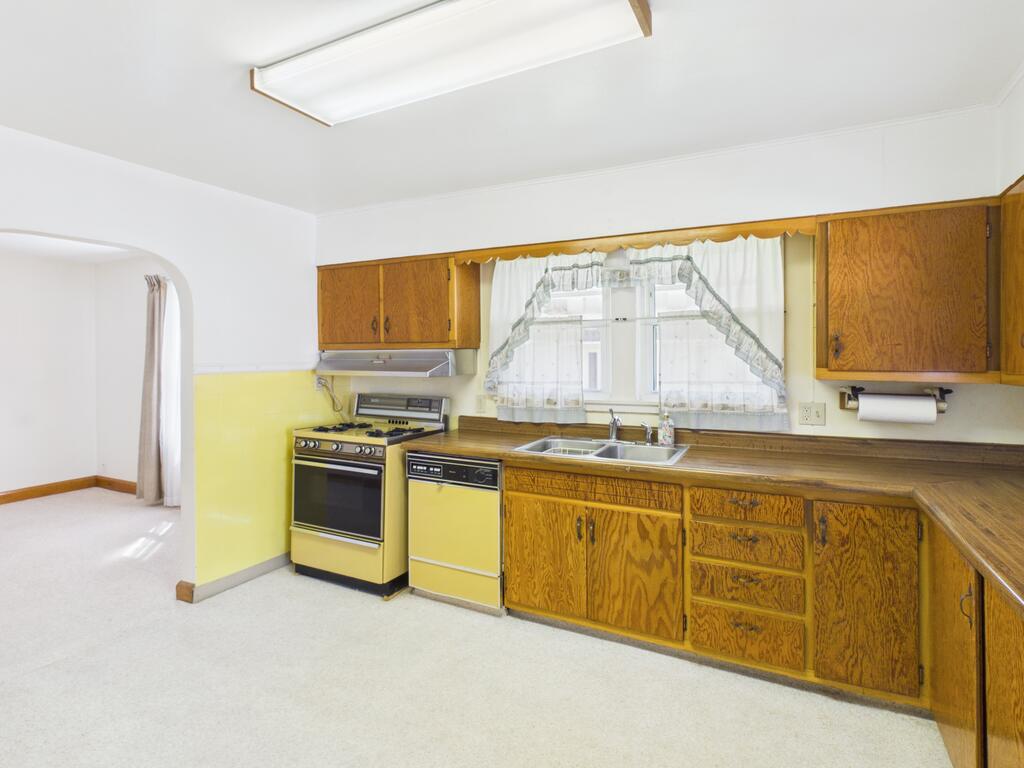 Kitchen with honey-colored wood cabinets, yellow walls, and a double-basin sink beneath a curtained window.