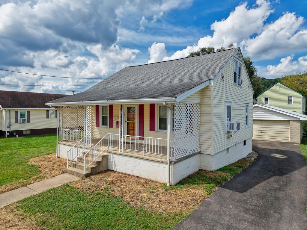 Light-colored two-story home with a covered lattice porch, red shutters, and a paved driveway.