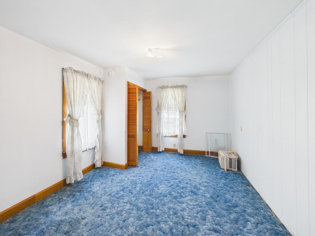 Empty room with blue carpet, two curtained windows, and an open louvered closet door.