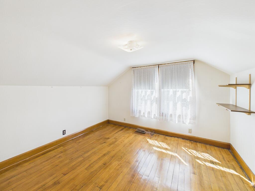 Empty room with hardwood floors, lace-curtained window, and wall-mounted shelves.