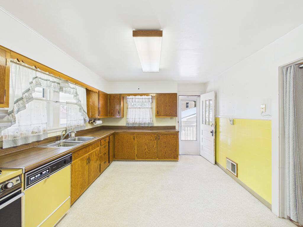 Kitchen with wood cabinets, a double-basin sink, yellow lower walls, and an open exterior door.