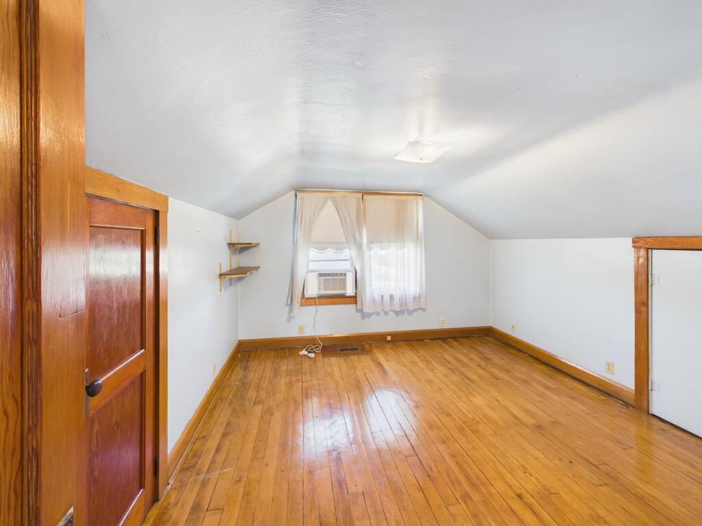 Empty room with hardwood floors, a sloped ceiling, and a window air conditioner.