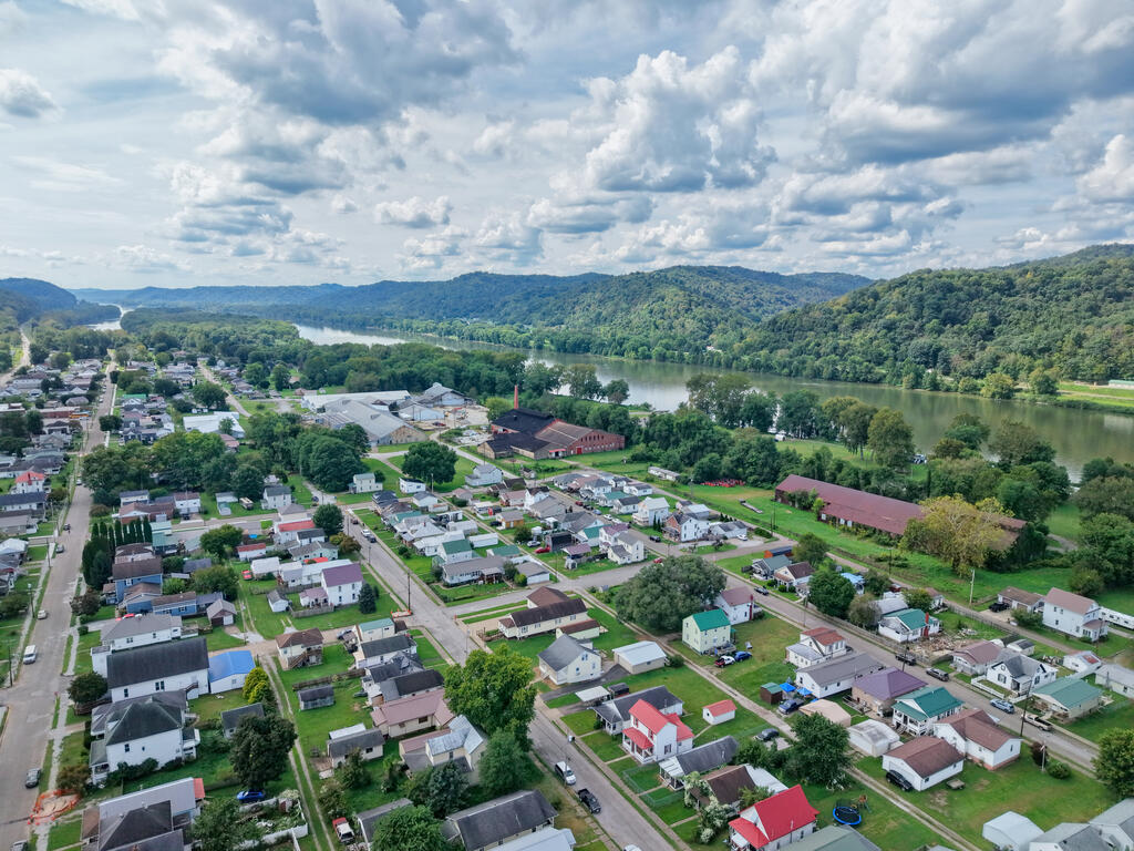 Aerial view of a riverside town, with wooded hills beyond the river.