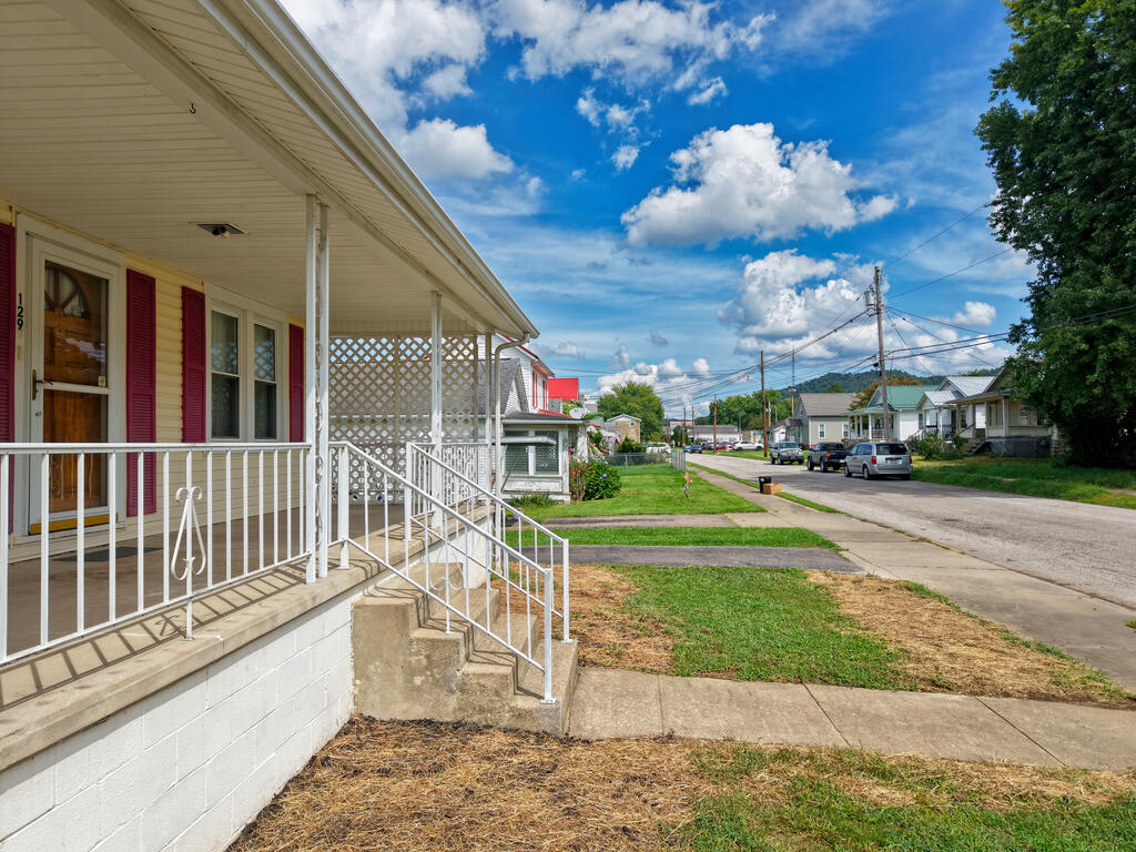 House with a covered porch, white railings, and red shutters beside a residential street.