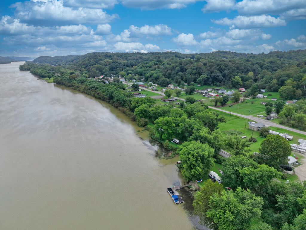 Aerial view of a riverfront lot with wooded shoreline, nearby homes, and a small dock.