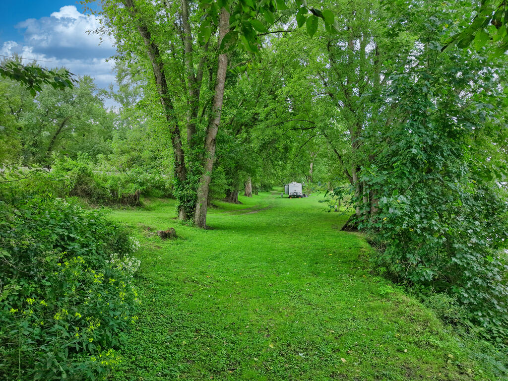 Grassy vacant lot surrounded by mature trees, with a small trailer in the distance.