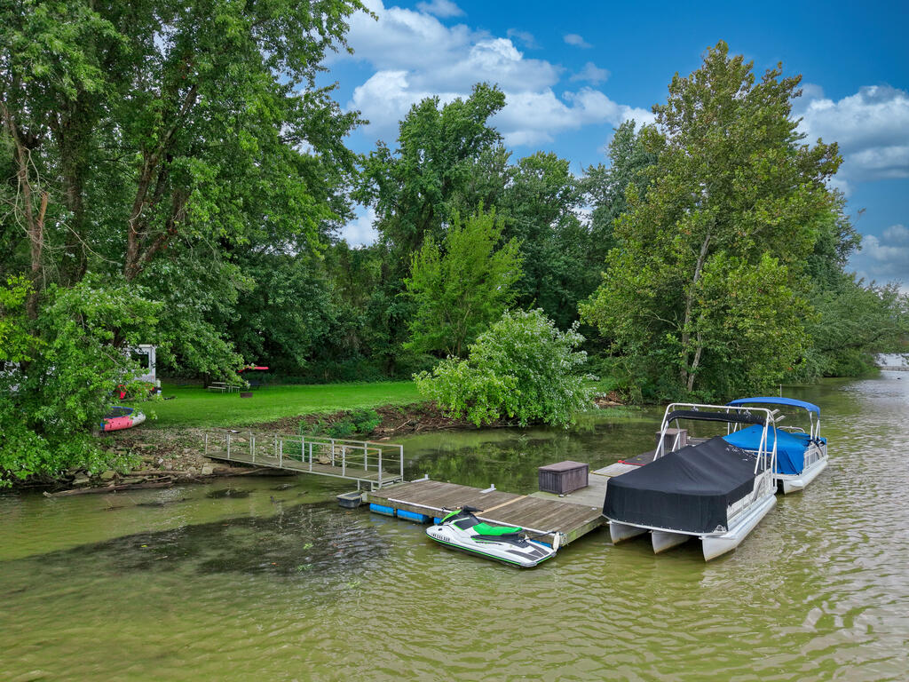 Riverfront lot with a dock, access ramp, and boats moored beside a wooded grassy shore.
