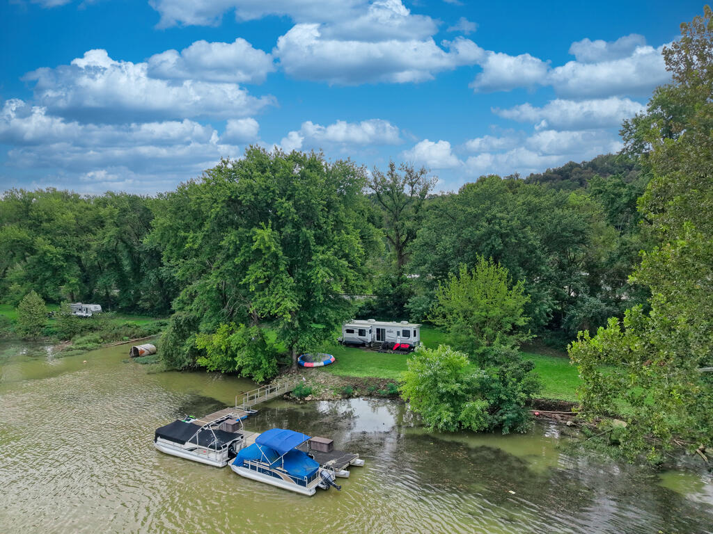 Aerial view of a wooded river lot with a dock, boats, and campers.
