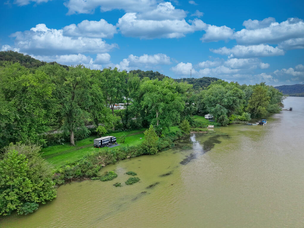 Aerial view of a wooded riverfront lot with grassy clearings, RVs, and small docks.