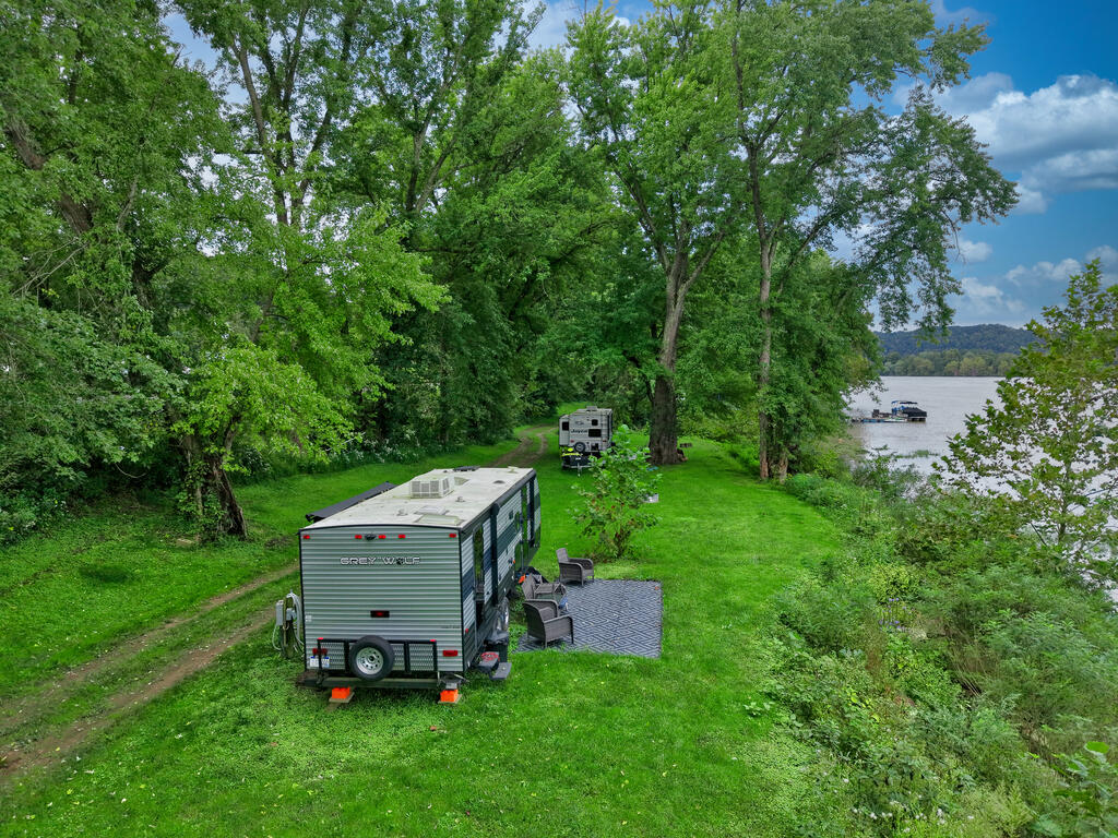 Grassy riverfront lot with two trailers beneath mature trees and a dock.