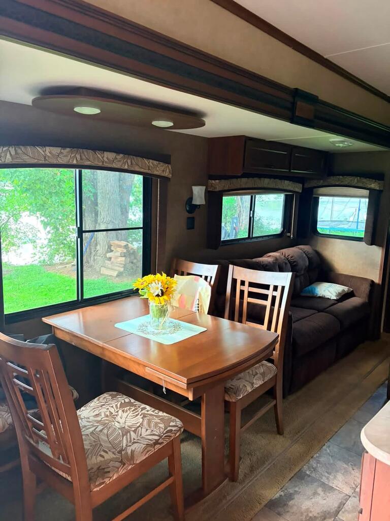 RV dining and living area with a wooden table, brown sofa, and large windows