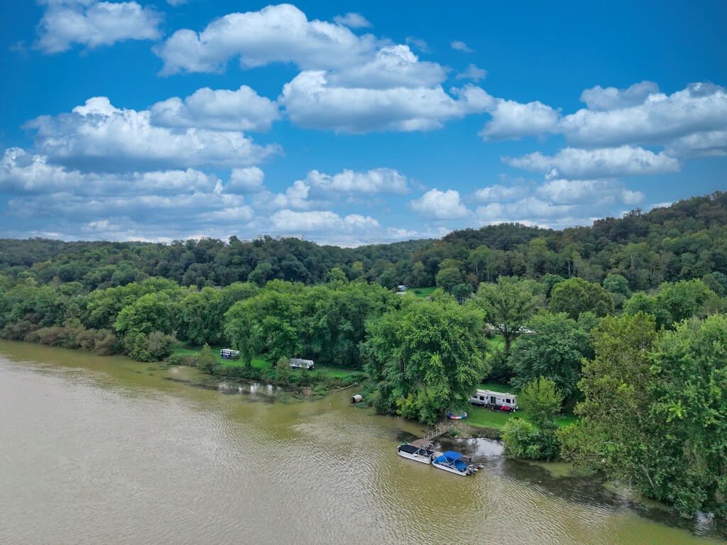Wooded riverfront lot with RVs and a small dock with boats along the riverbank.
