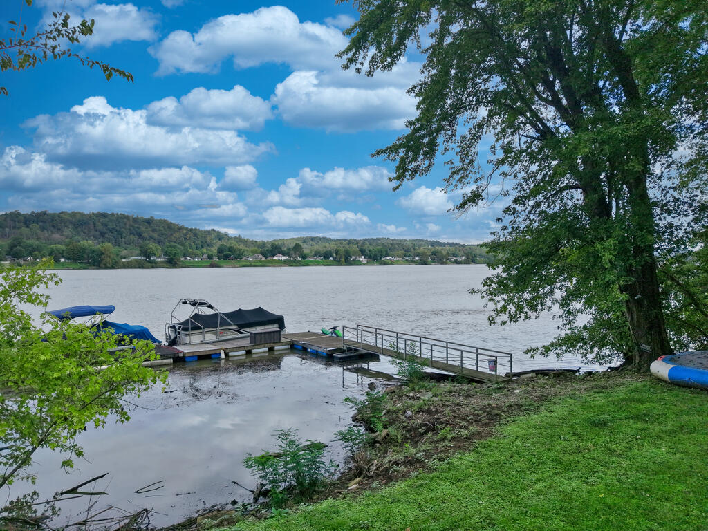Riverfront lot with a dock and boats beside a grassy, tree-lined shoreline.