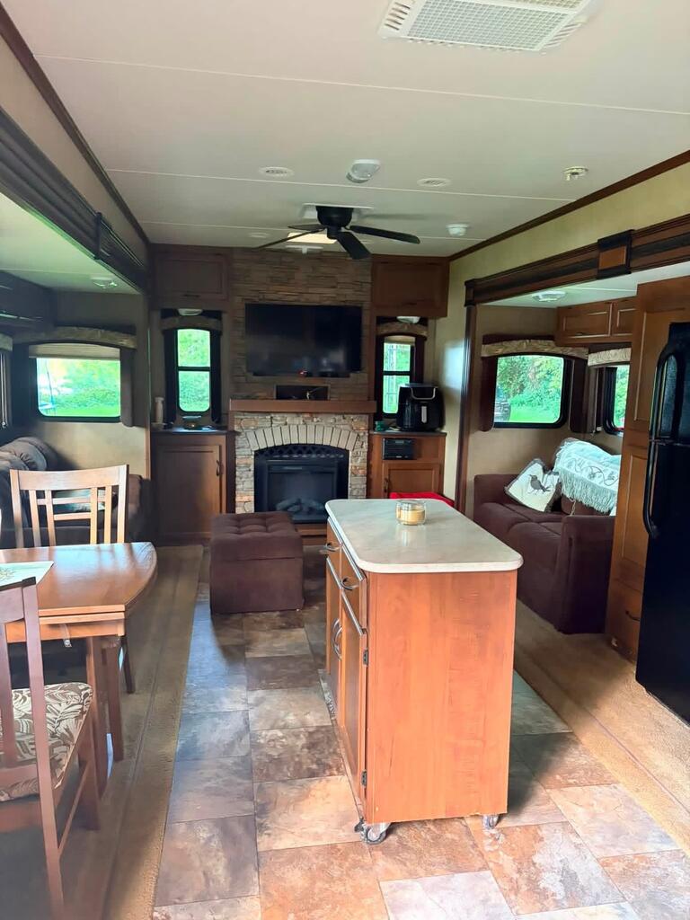 Furnished RV living area with a kitchen island and stone fireplace.