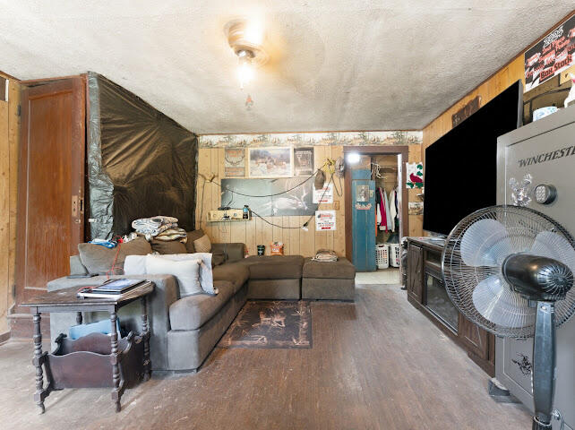 Living room with a sectional sofa, wood-paneled walls, a standing fan, and a large safe.