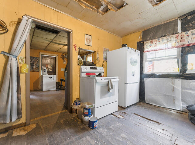 Laundry room with a washer, dryer, and refrigerator beneath a damaged ceiling.