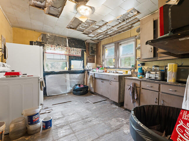 Worn kitchen with missing ceiling panels, exposed insulation, and old cabinets.