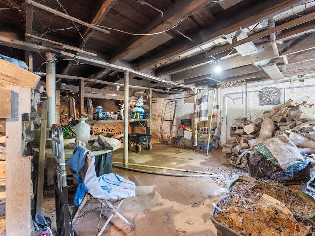 Unfinished basement with exposed beams, workshop shelving, and piles of stored wood.
