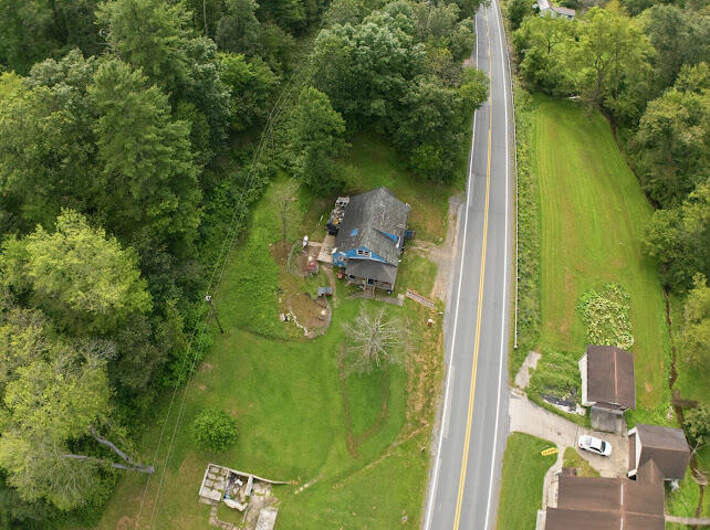 Aerial view of a house on a grassy lot beside a two-lane road, surrounded by trees.