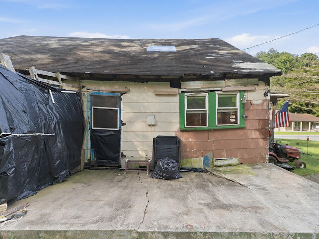 Weathered house with green-trimmed windows, a tarp-covered section, and a wide concrete driveway.