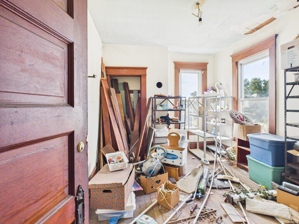 Cluttered room with wood-trimmed windows, storage bins, loose materials, and a damaged ceiling.