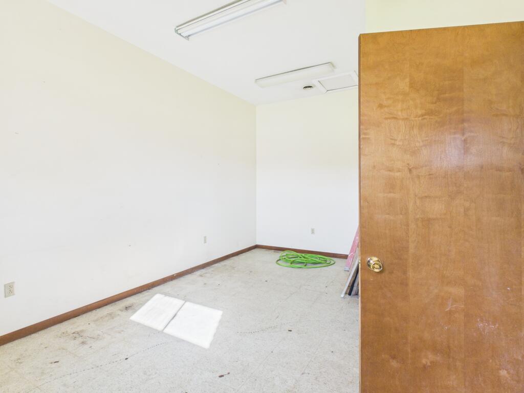 Empty room with fluorescent ceiling lights, a green hose on the floor, and an open wooden door.