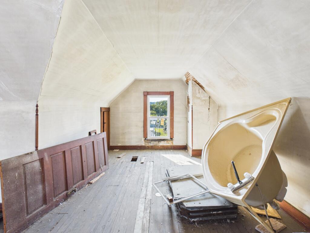 Deteriorated attic room with sloped ceiling, worn floorboards, and a bathtub tipped on its side.