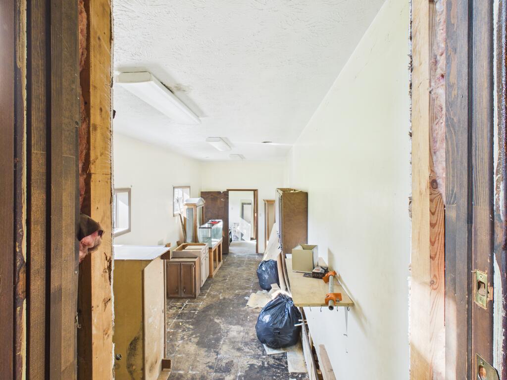 Unfinished narrow interior with exposed framing, debris, and cabinets along the sides.