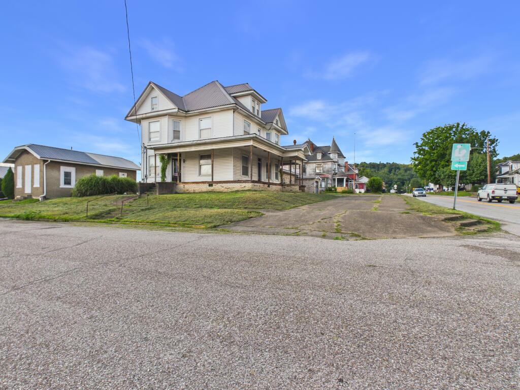 White two-story house with a wraparound porch and steep roof on a corner lot.