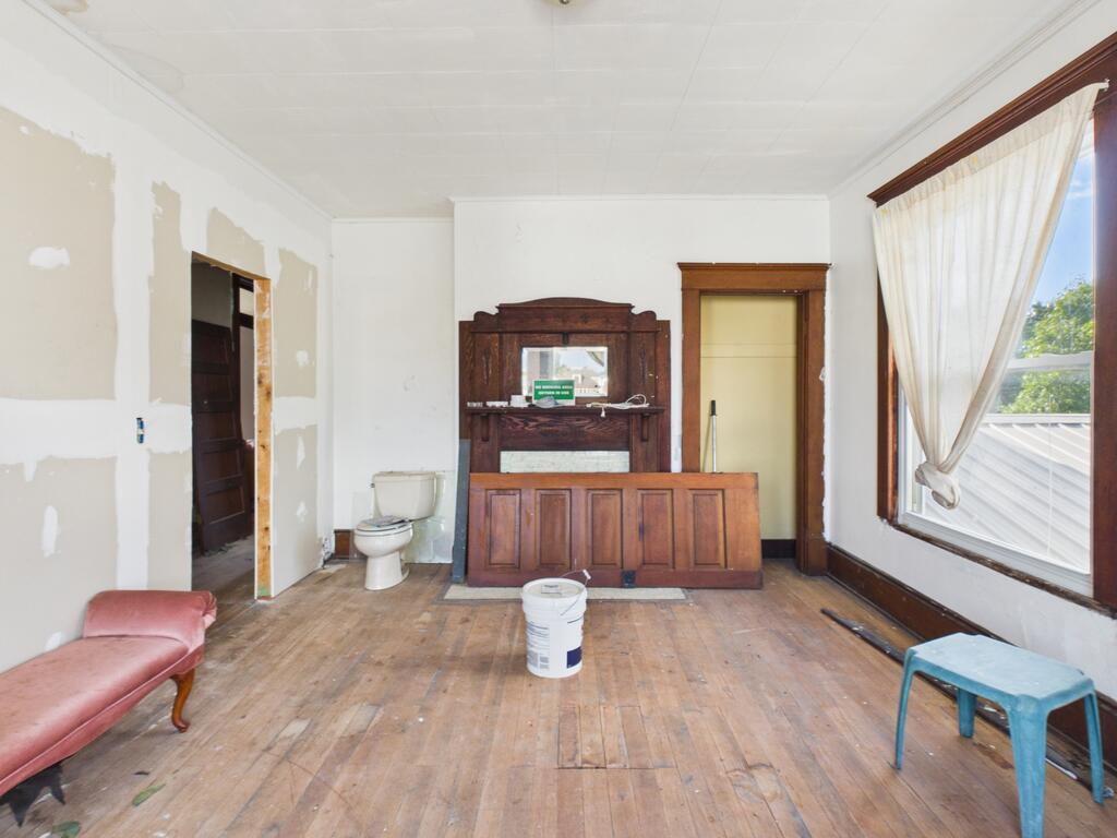 Unfinished interior room with patched drywall, a toilet, and worn wood flooring.