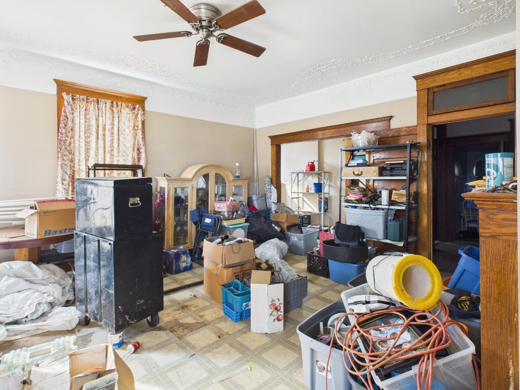 Cluttered interior room with ornate ceiling trim, patterned tile flooring, and dark wood doorway trim.