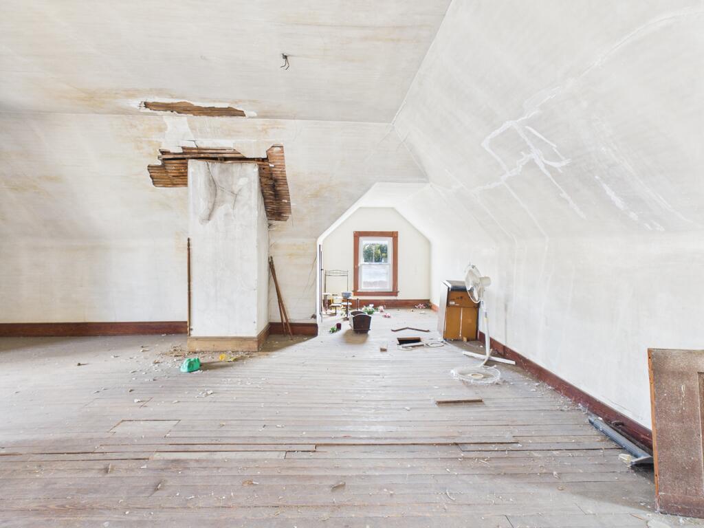 Vacant attic room with exposed ceiling boards, worn plank flooring, and a small window.