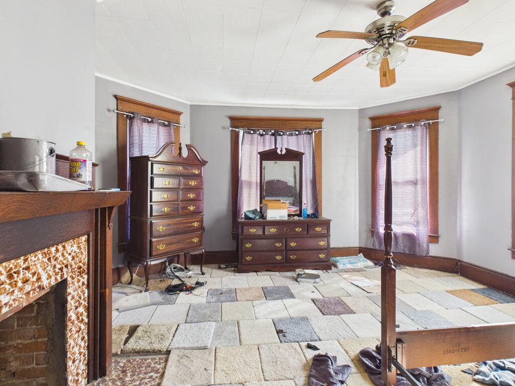Bedroom with patchwork tile flooring, dark wood dresser, purple curtains, and tiled fireplace.