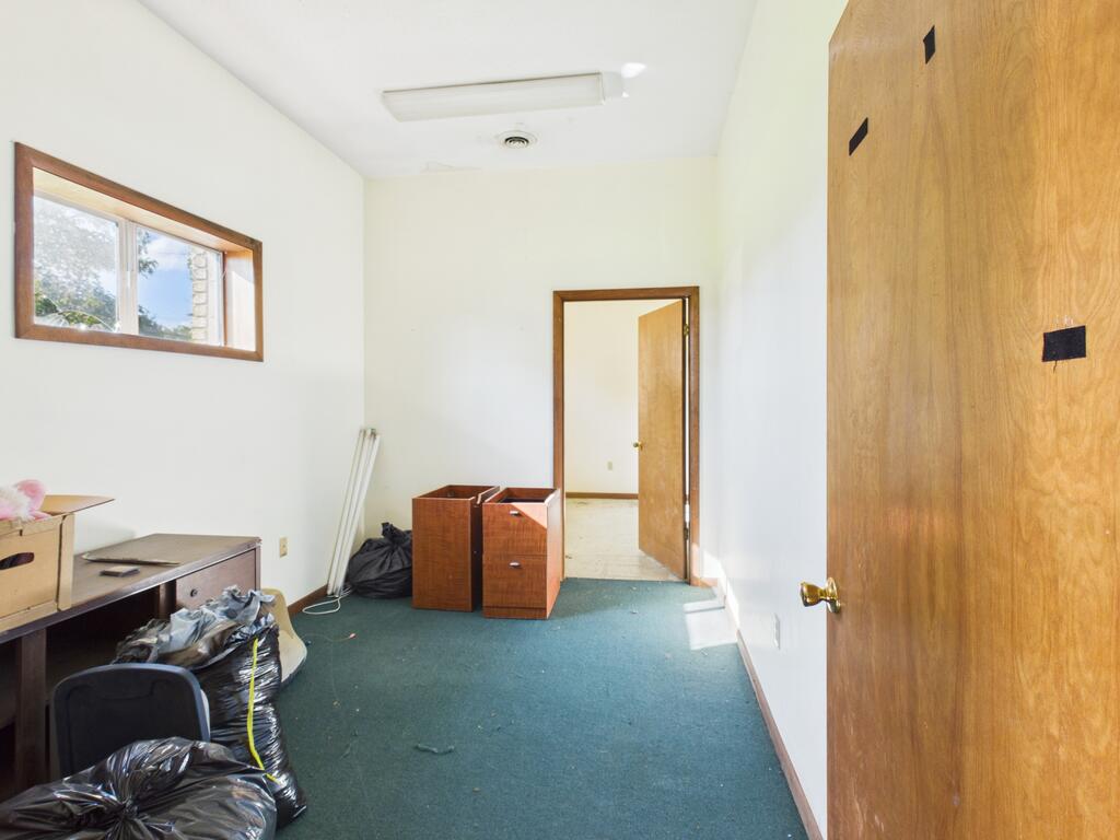 Interior room with green carpet, a small window, wooden doors, and discarded furniture and bags.