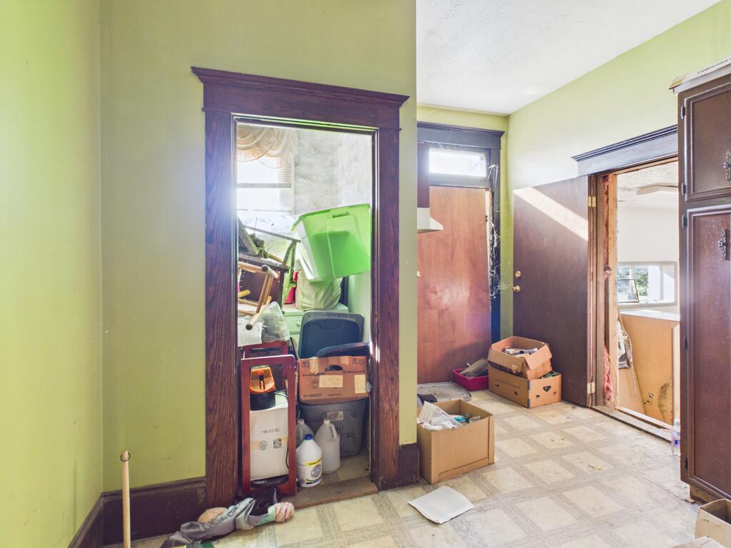 Cluttered interior room with pale green walls, tiled floor, and dark wood door frames.