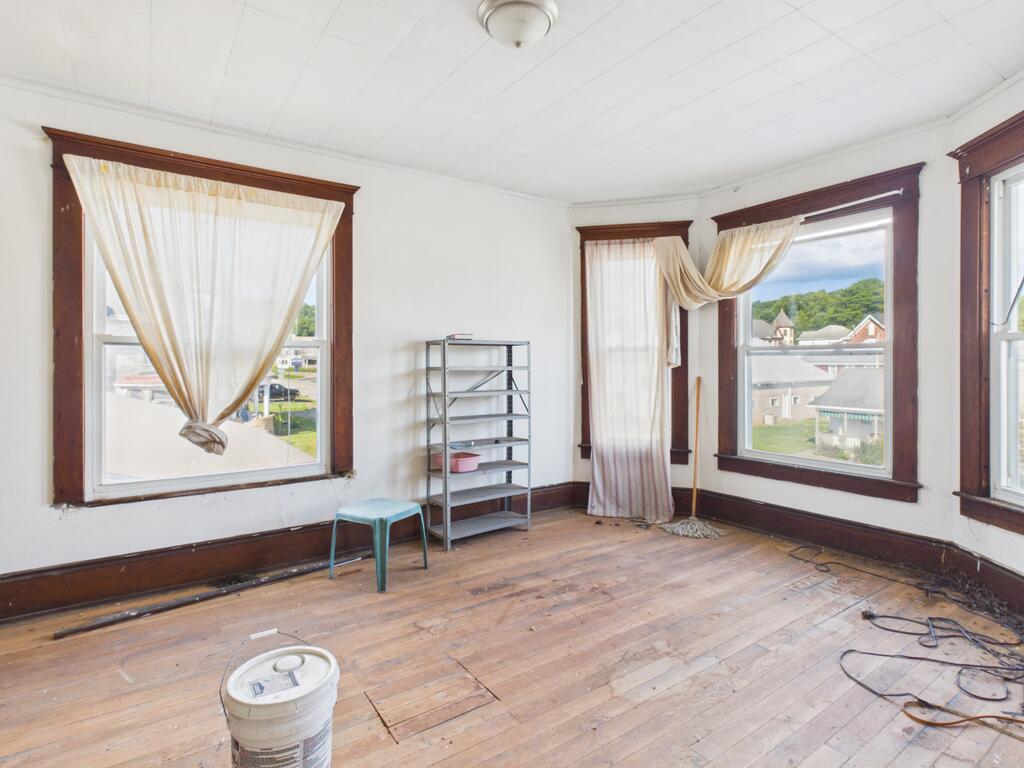 Vacant room with worn hardwood floors, dark wood window trim, and several curtained windows.