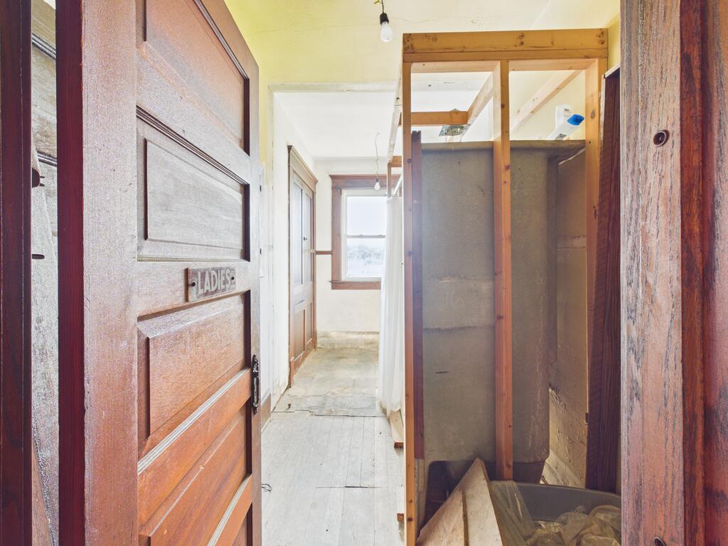 Narrow hallway with a wooden LADIES door, exposed framing, and debris.