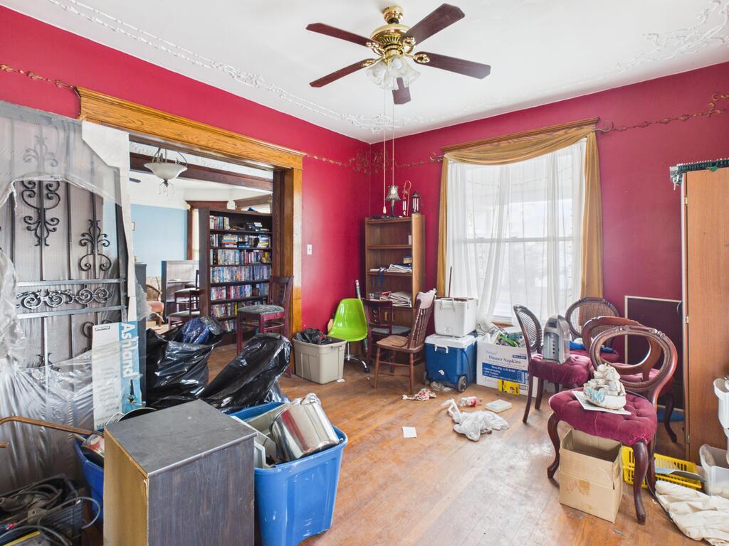 Red-walled room with a ceiling fan, wood flooring, and furniture, bins, and boxes throughout.
