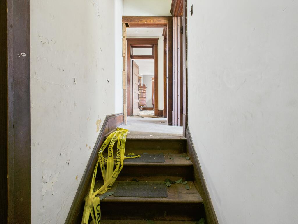 Worn wooden stairs lead up to a hallway with open doorways and yellow caution tape.